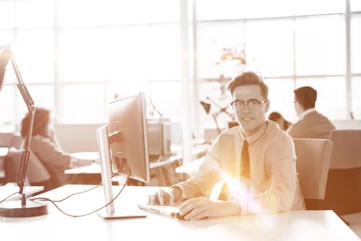 Young businessman programer in big bright office at work using computer