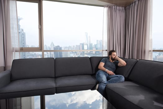 young man sitting on sofa and using a mobile phone  near the window at home