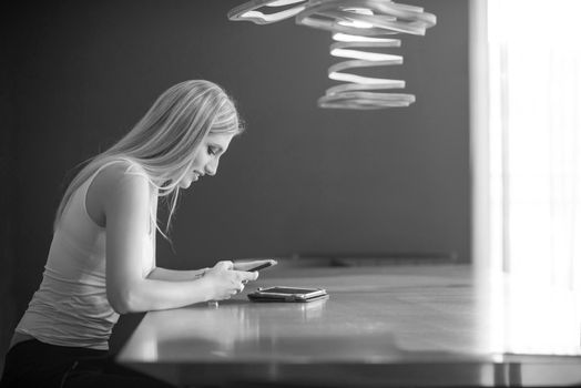 young happy woman sitting at the table and using mobile phone at luxury home