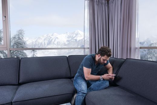 young man sitting on sofa and using a mobile phone  near the window at home