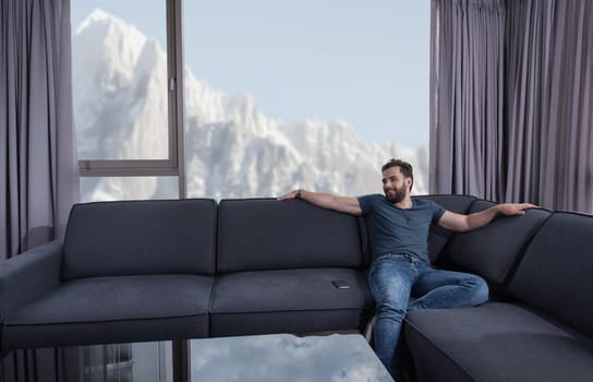 young man sitting on sofa and using a mobile phone  near the window at home