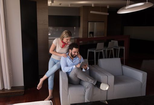 Young couple relaxing at  home using tablet computers reading in the living room on the sofa couch.