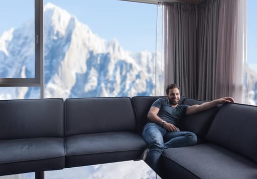 young man sitting on sofa and using a mobile phone  near the window at home