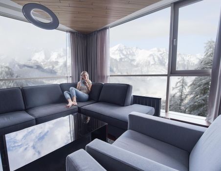 Young beautiful girl enjoying music through headphones, laying on sofa near the window at home