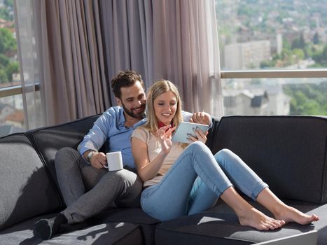 Young couple relaxing at  home using tablet computers reading in the living room on the sofa couch.