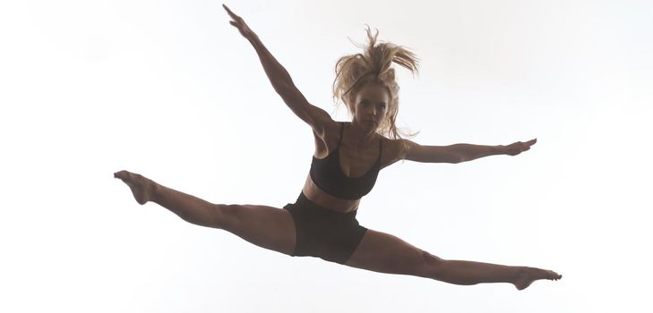 young beautiful female sporty dancer in black tights performing modern style ballet making acrobatic elements   female ballet dancer in art performance in front of white background