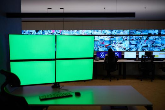 Empty interior of big modern security system control room with blank green screens, workstation with multiple displays, monitoring room with at security data center  Empty office, desk, and chairs at a main CCTV security data center