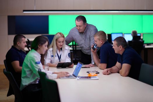 Group of security guards sitting and having briefing In the system control room  They're working in security data center surrounded by multiple Screens