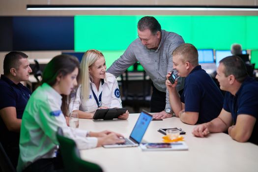 Group of security guards sitting and having briefing In the system control room  They're working in security data center surrounded by multiple Screens