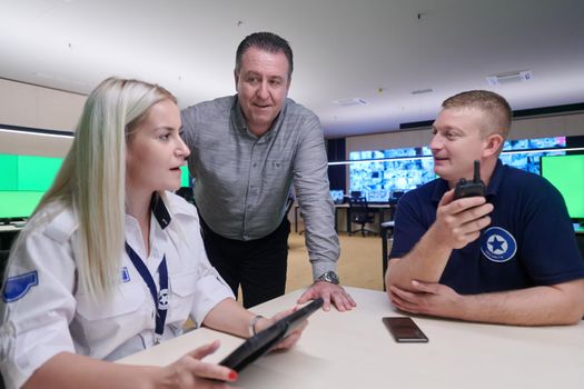 Group of security guards sitting and having briefing In the system control room  They're working in security data center surrounded by multiple Screens