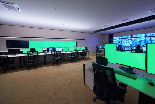 Empty interior of big modern security system control room with blank green screens, workstation with multiple displays, monitoring room with at security data center  Empty office, desk, and chairs at a main CCTV security data center