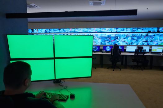 Male security operator working in a data system control room offices Technical Operator Working at  workstation with multiple displays, security guard working on multiple green blank screens  Male computer operator monitoring from a security center