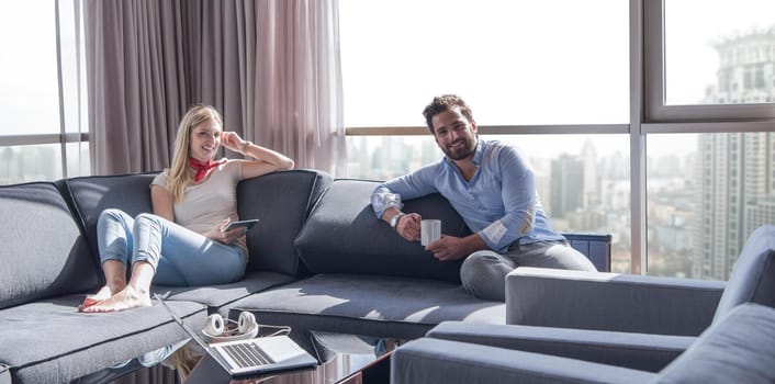 Young couple relaxing at  home using tablet computer reading in the living room near the window on the sofa couch.