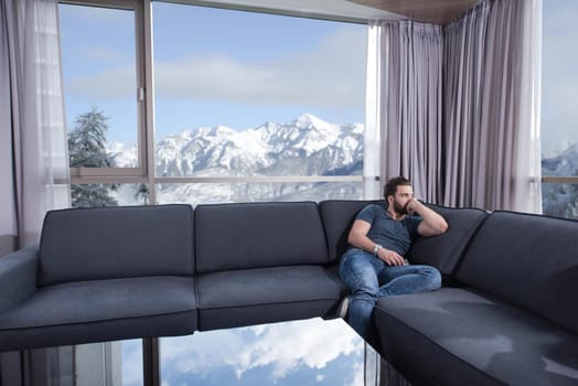 young man sitting on sofa and using a mobile phone  near the window at home