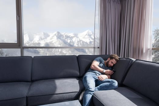 young man sitting on sofa and using a mobile phone  near the window at home