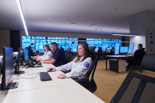 Group of Security data center operators working in a CCTV monitoring room looking on multiple monitors  Officers Monitoring Multiple Screens for Suspicious Activities  Team working on the System Control Room