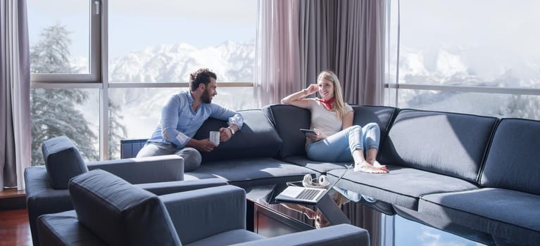 Young couple relaxing at  home using tablet computer reading in the living room near the window on the sofa couch.