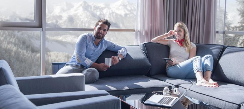 Young couple relaxing at  home using tablet computer reading in the living room near the window on the sofa couch.