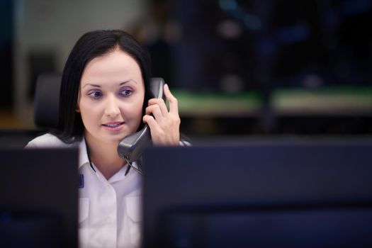 Female security guard operator talking on the phone while working at workstation with multiple displays Security guards working on multiple monitors