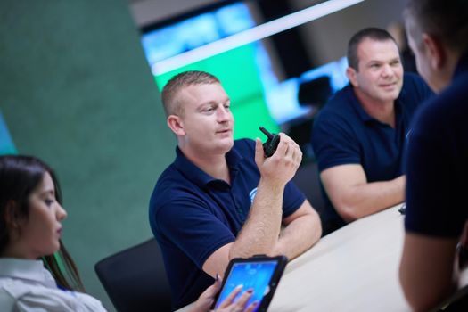 Group of security guards sitting and having briefing In the system control room  They're working in security data center surrounded by multiple Screens