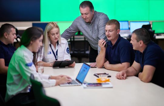 Group of security guards sitting and having briefing In the system control room  They're working in security data center surrounded by multiple Screens