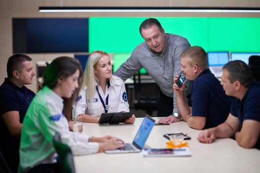 Group of security guards sitting and having briefing In the system control room  They're working in security data center surrounded by multiple Screens