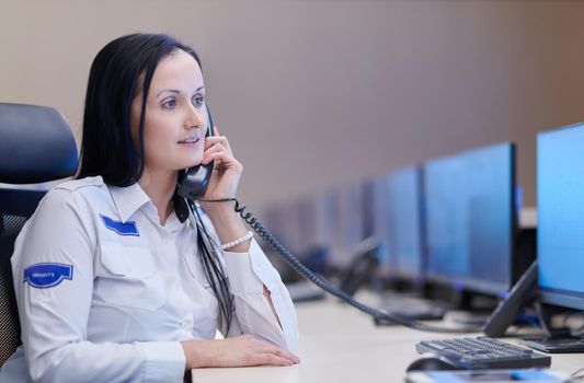 Female security guard operator talking on the phone while working at workstation with multiple displays Security guards working on multiple monitors