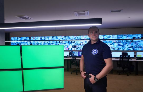 portrait of young male security operator working in a data system control room Working at workstation with multiple displays, security guard working on multiple monitors  Male computer operator monitoring from a security center
