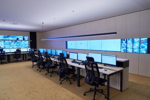 Empty interior of big modern security system control room, workstation with multiple displays, monitoring room with at security data center  Empty office, desk, and chairs at a main CCTV security data center