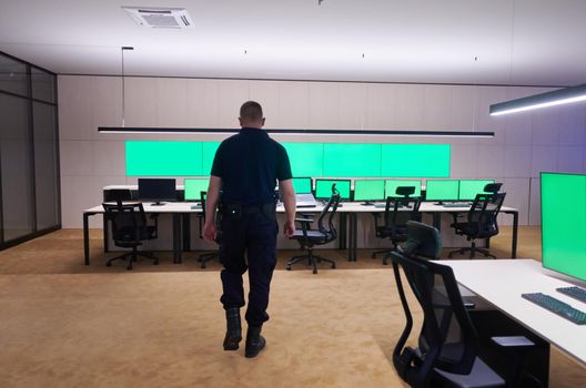 young male security operator walking through data system control room Working at workstation with multiple displays, security guard working on multiple monitors  Male computer operator monitoring from a security center