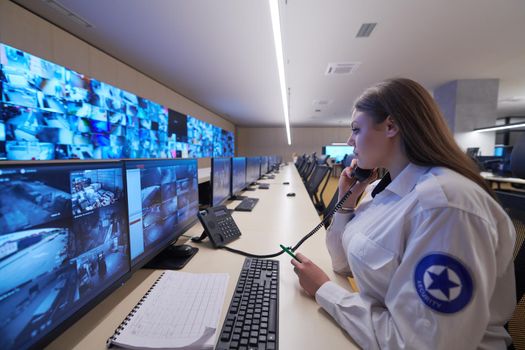 Female security guard operator talking on the phone while working at workstation with multiple displays Security guards working on multiple monitors