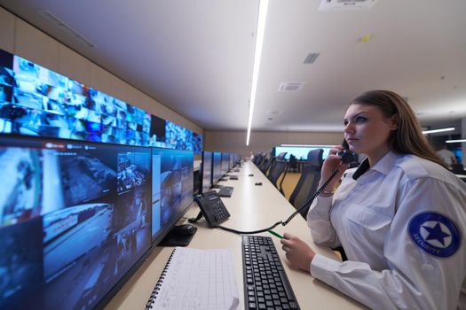 Female security guard operator talking on the phone while working at workstation with multiple displays Security guards working on multiple monitors