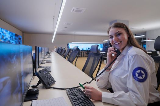 Female security guard operator talking on the phone while working at workstation with multiple displays Security guards working on multiple monitors