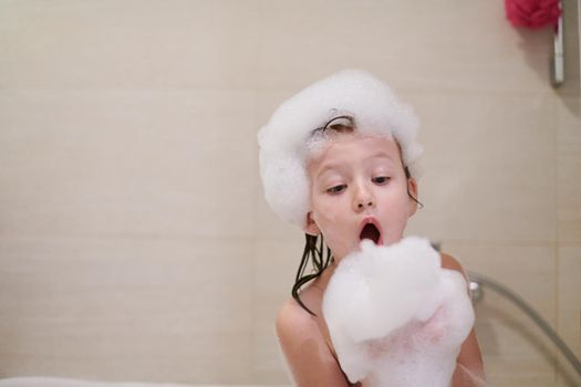 little girl playing with soap foam in bath during coronavirus stay at home pandemic quarantine