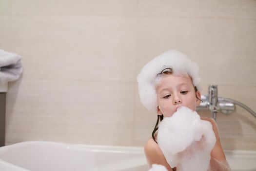 little girl playing with soap foam in bath during coronavirus stay at home pandemic quarantine