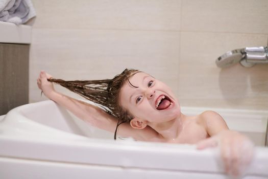 little girl playing with soap foam in bath during coronavirus stay at home pandemic quarantine