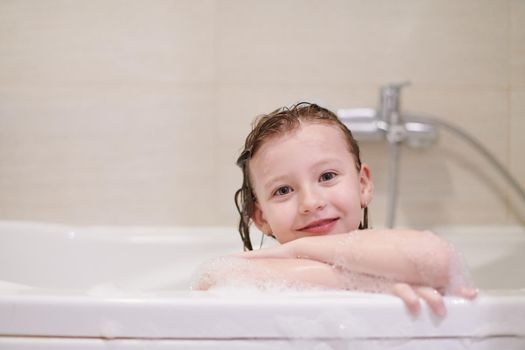 little girl playing with soap foam in bath during coronavirus stay at home pandemic quarantine