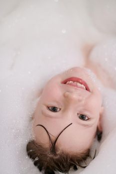 little girl playing with soap foam in bath during coronavirus stay at home pandemic quarantine