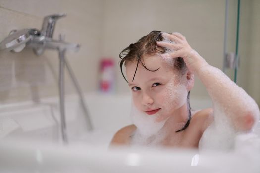 little girl playing with soap foam in bath during coronavirus stay at home pandemic quarantine