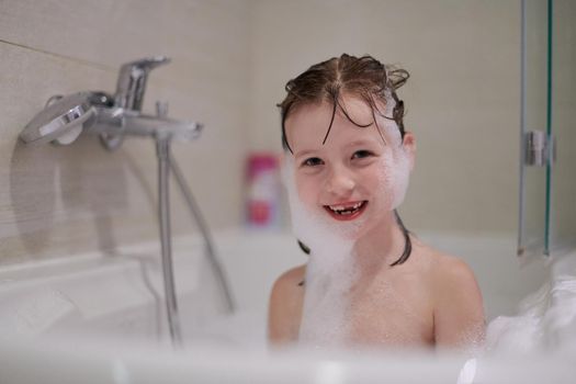 little girl playing with soap foam in bath during coronavirus stay at home pandemic quarantine