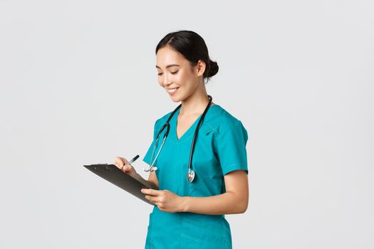 Healthcare workers, preventing virus, quarantine campaign concept. Beautiful smiling asian doctor, nurse running checkup in hospital, looking at clipboard with patient results, examine people.