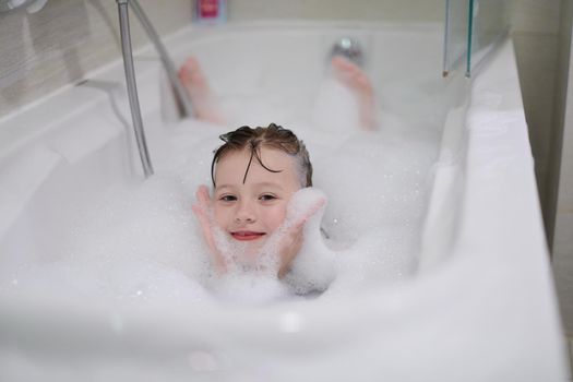 little girl playing with soap foam in bath during coronavirus stay at home pandemic quarantine