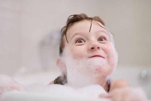 little girl playing with soap foam in bath during coronavirus stay at home pandemic quarantine