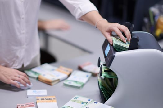 Bank employees using money counting machine while sorting and counting paper banknotes inside bank vault. Large amounts of money in the bank