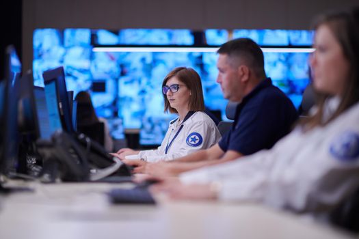 Group of Security data center operators working in a CCTV monitoring room looking on multiple monitors  Officers Monitoring Multiple Screens for Suspicious Activities  Team working on the System Control Room