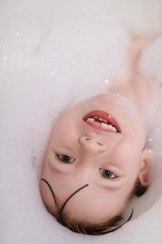 little girl playing with soap foam in bath during coronavirus stay at home pandemic quarantine