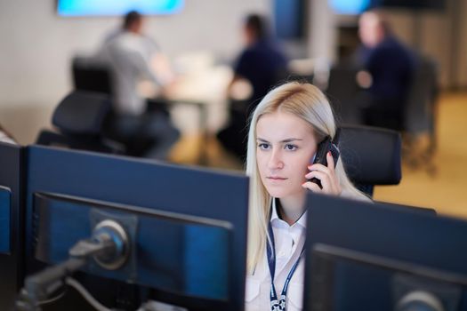 Female security guard operator talking on the phone while working at workstation with multiple displays Security guards working on multiple monitors