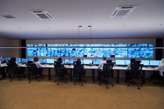 Group of Security data center operators working in a CCTV monitoring room looking on multiple monitors  Officers Monitoring Multiple Screens for Suspicious Activities  Team working on the System Control Room