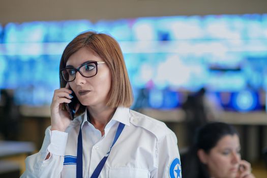 Female security guard operator talking on the phone while working at workstation with multiple displays Security guards working on multiple monitors