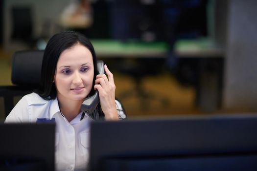 Female security guard operator talking on the phone while working at workstation with multiple displays Security guards working on multiple monitors